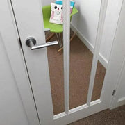 White door with a pet gate in a room with a green chair and colorful items.