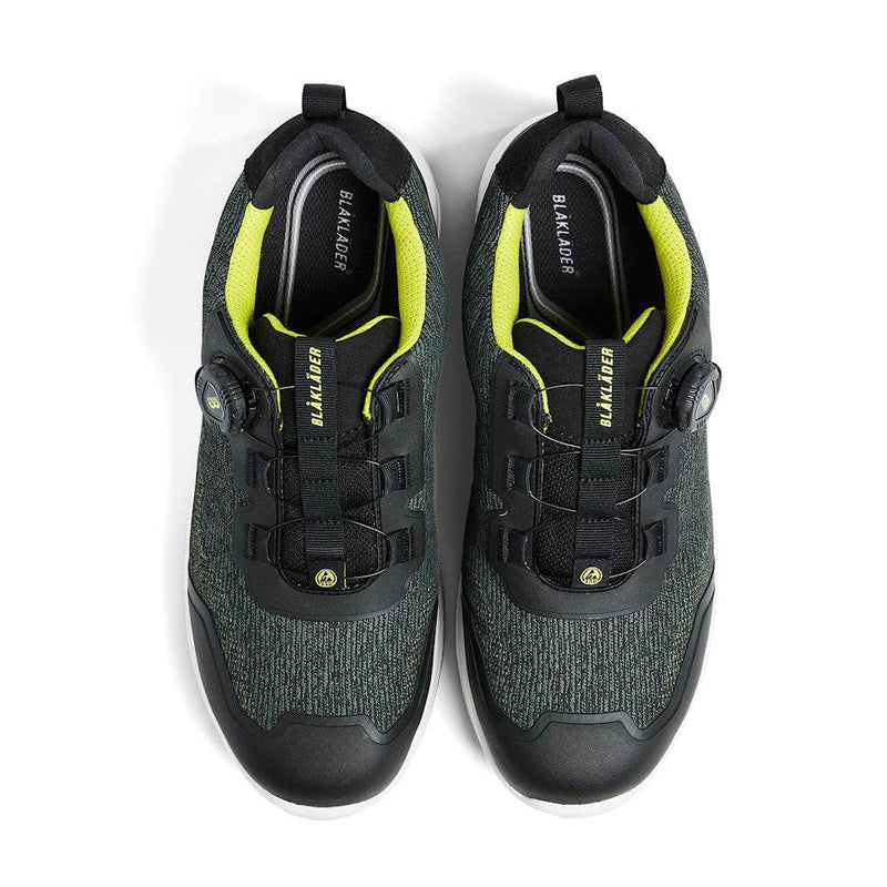 Pair of black and green safety work shoes with yellow accents on a white background
