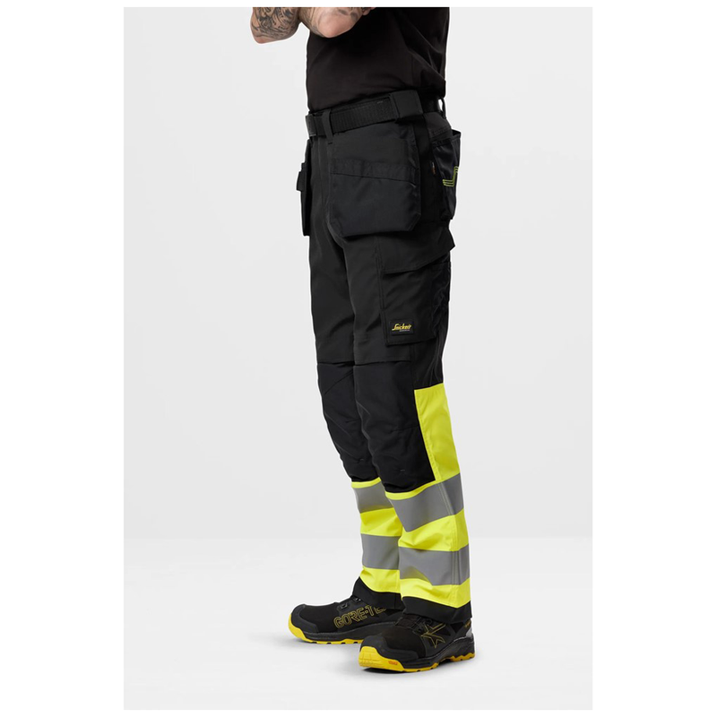 Person wearing black and yellow work pants with reflective stripes on a white background
